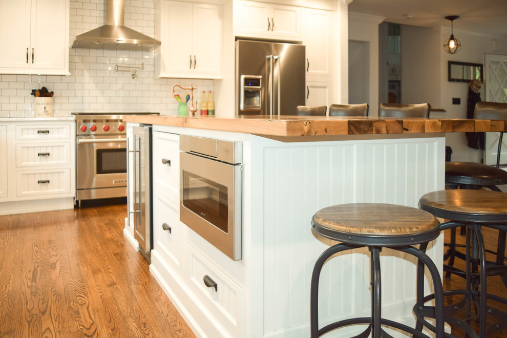 ニューヨークにある広いカントリー風のおしゃれなキッチン (エプロンフロントシンク、インセット扉のキャビネット、白いキャビネット、木材カウンター、白いキッチンパネル、サブウェイタイルのキッチンパネル、シルバーの調理設備、無垢フローリング) の写真