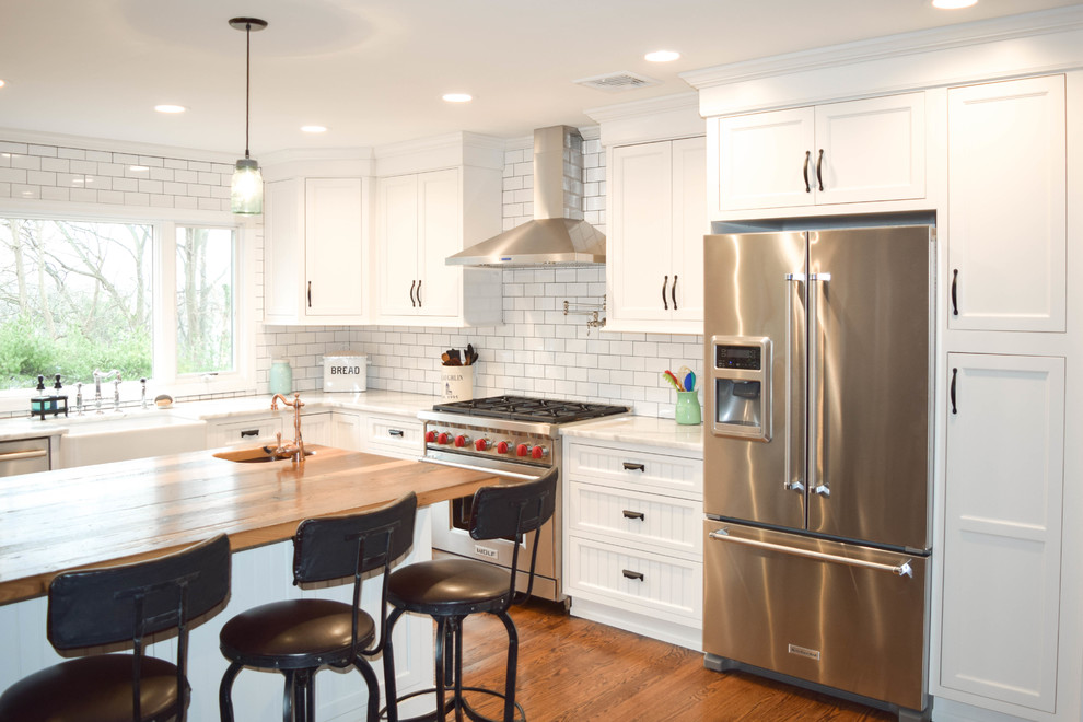 Large farmhouse l-shaped medium tone wood floor eat-in kitchen photo in New York with a farmhouse sink, beaded inset cabinets, white cabinets, wood countertops, white backsplash, subway tile backsplash, stainless steel appliances and an island