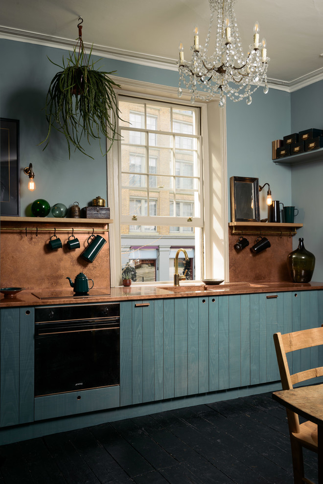 ロンドンにあるお手頃価格の中くらいなエクレクティックスタイルのおしゃれなダイニングキッチン (一体型シンク、フラットパネル扉のキャビネット、青いキャビネット、銅製カウンター、オレンジのキッチンパネル、パネルと同色の調理設備、塗装フローリング、アイランドなし、黒い床、オレンジのキッチンカウンター) の写真