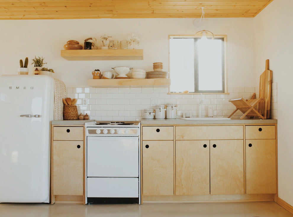 Trendy single-wall concrete floor and gray floor kitchen photo in Los Angeles with a drop-in sink, flat-panel cabinets, light wood cabinets, concrete countertops, white backsplash, subway tile backsplash, white appliances and gray countertops