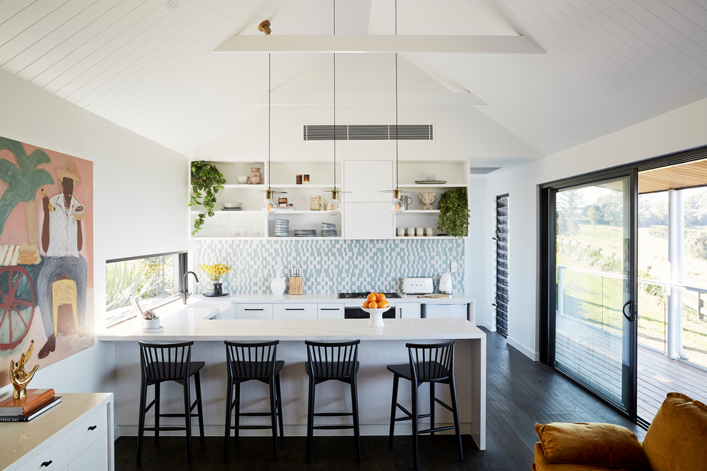 Open concept kitchen - coastal u-shaped dark wood floor and black floor open concept kitchen idea in Other with a farmhouse sink, flat-panel cabinets, white cabinets, multicolored backsplash, paneled appliances, a peninsula and white countertops
