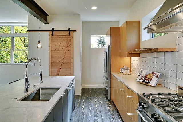 Inredning av ett lantligt linjärt kök med öppen planlösning, med en undermonterad diskho, släta luckor, skåp i mellenmörkt trä, vitt stänkskydd, rostfria vitvaror, mörkt trägolv, en köksö och svart golv