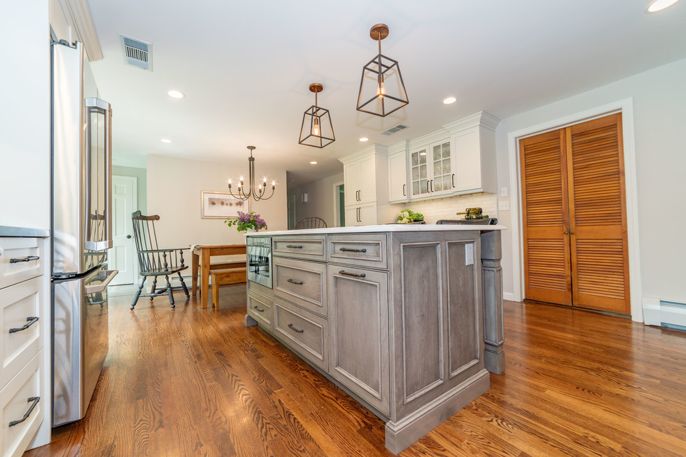 Example of a large country l-shaped dark wood floor and brown floor eat-in kitchen design in Bridgeport with an undermount sink, recessed-panel cabinets, white cabinets, quartz countertops, white backsplash, subway tile backsplash, stainless steel appliances, an island and black countertops