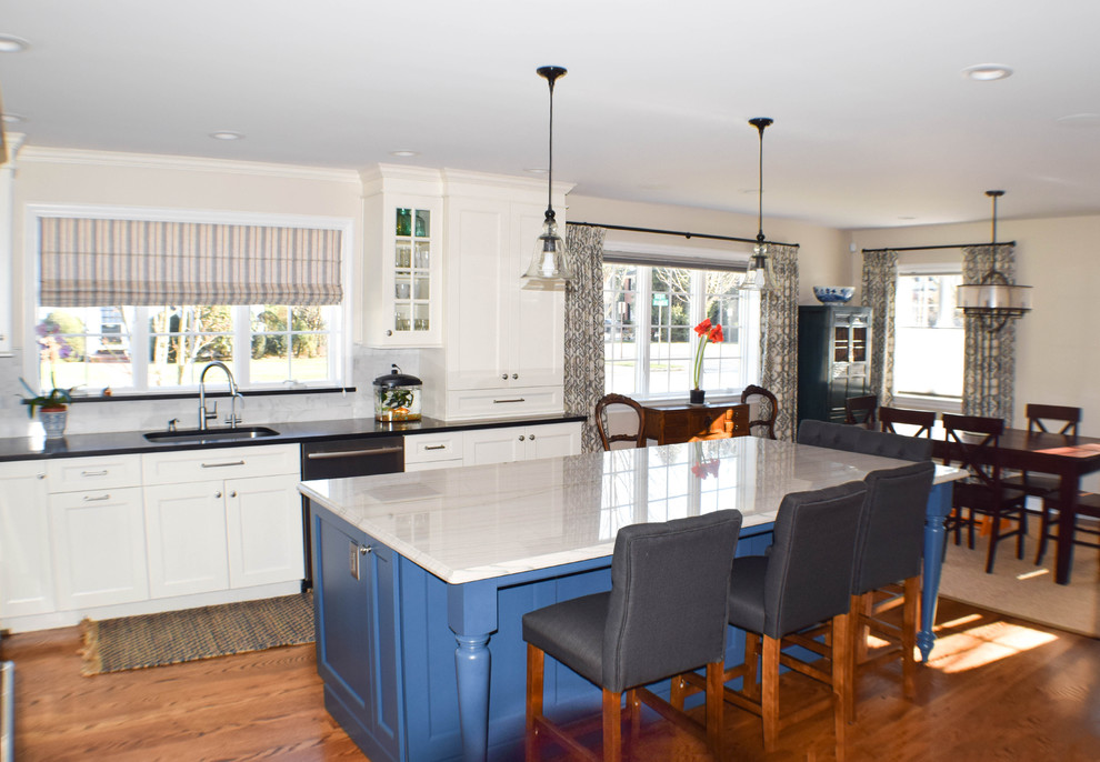 Example of a large classic u-shaped medium tone wood floor eat-in kitchen design in New York with a drop-in sink, recessed-panel cabinets, white cabinets, quartzite countertops, gray backsplash, stone tile backsplash, stainless steel appliances and an island