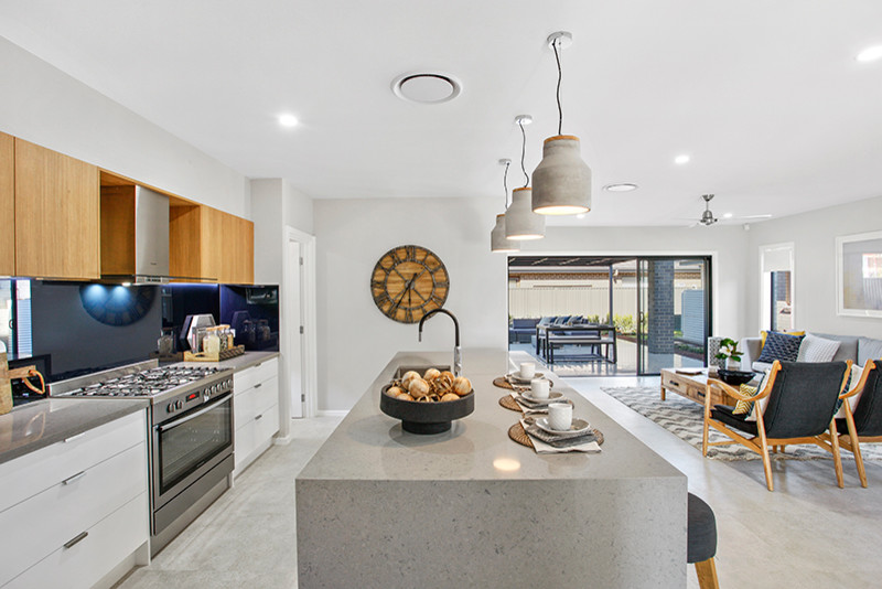 На фото: кухня-гостиная среднего размера в современном стиле с светлыми деревянными фасадами, столешницей из акрилового камня, синим фартуком и островом с