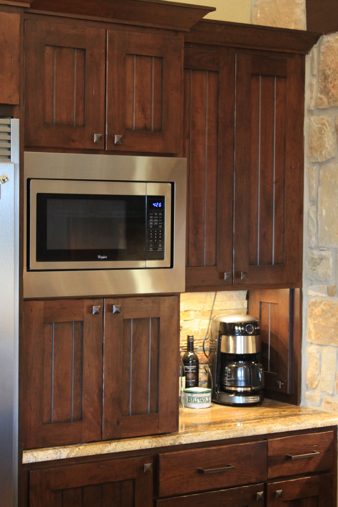 Bild på ett rustikt kök, med en rustik diskho, luckor med profilerade fronter, skåp i mörkt trä, granitbänkskiva, rostfria vitvaror, betonggolv och en halv köksö