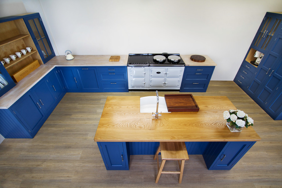Mittelgroße Klassische Küche in L-Form mit Unterbauwaschbecken, Kassettenfronten, blauen Schränken, Arbeitsplatte aus Holz, weißen Elektrogeräten, braunem Holzboden und Kücheninsel in Sonstige