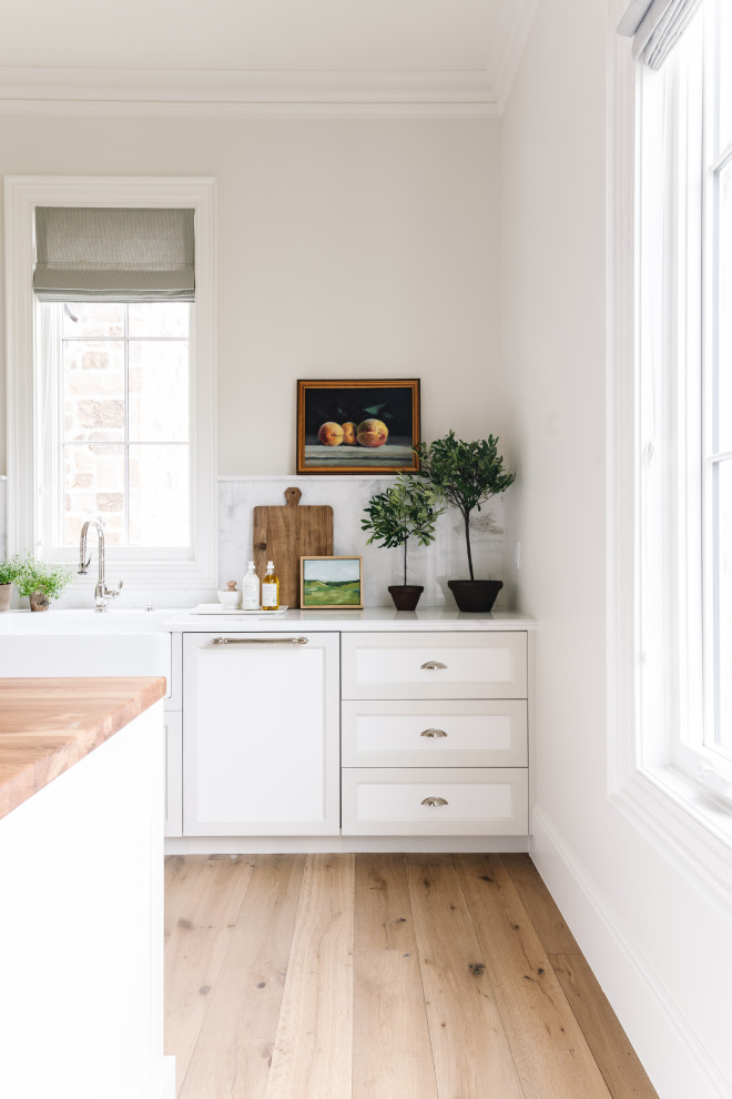 Example of a classic light wood floor kitchen pantry design in Salt Lake City with a farmhouse sink, shaker cabinets, white cabinets, marble countertops, white backsplash, stainless steel appliances, an island and white countertops