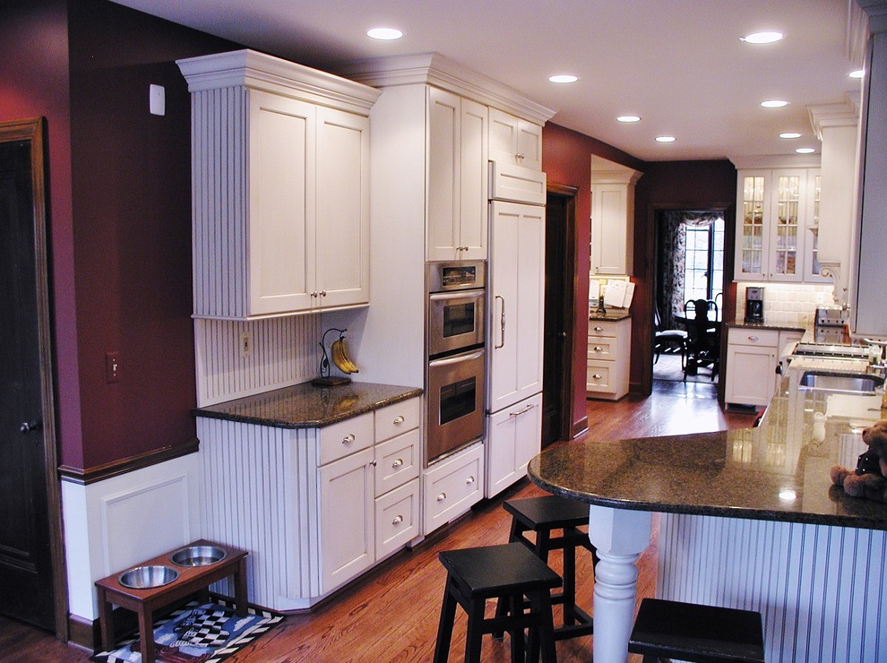Example of a large classic galley medium tone wood floor eat-in kitchen design in Detroit with white cabinets, granite countertops, stainless steel appliances, a double-bowl sink, shaker cabinets, beige backsplash, stone tile backsplash and no island