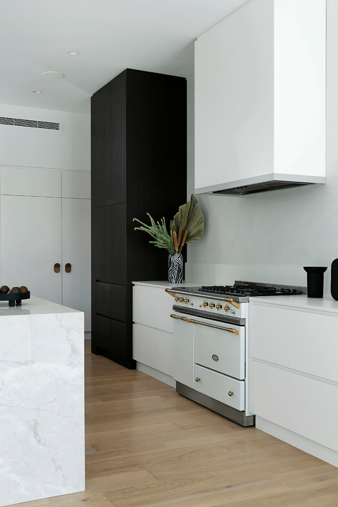 Inspiration för ett stort funkis vit vitt kök, med vita skåp, marmorbänkskiva, vitt stänkskydd, rostfria vitvaror, mellanmörkt trägolv, en köksö, släta luckor och beiget golv