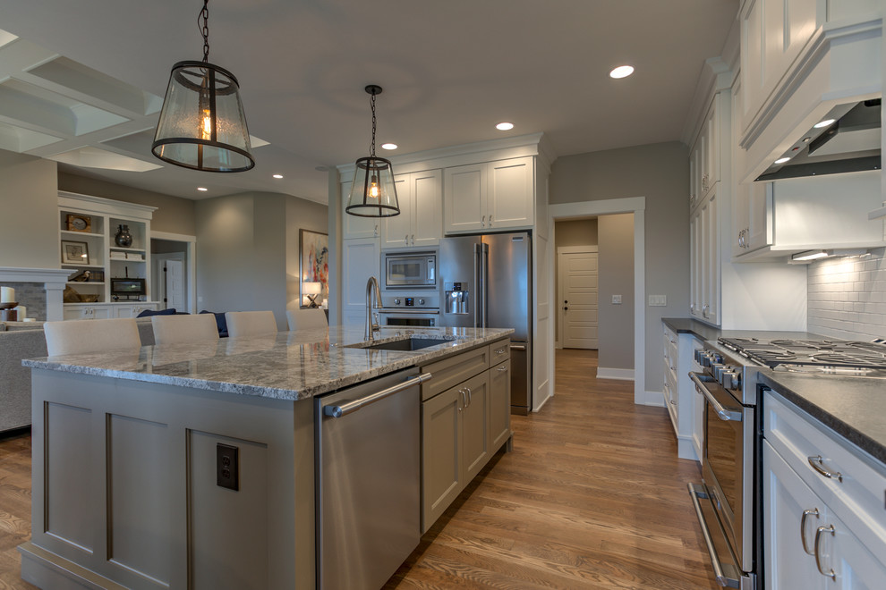 Example of a mid-sized transitional l-shaped medium tone wood floor and beige floor eat-in kitchen design in Omaha with an undermount sink, recessed-panel cabinets, white cabinets, granite countertops, white backsplash, subway tile backsplash, stainless steel appliances and an island