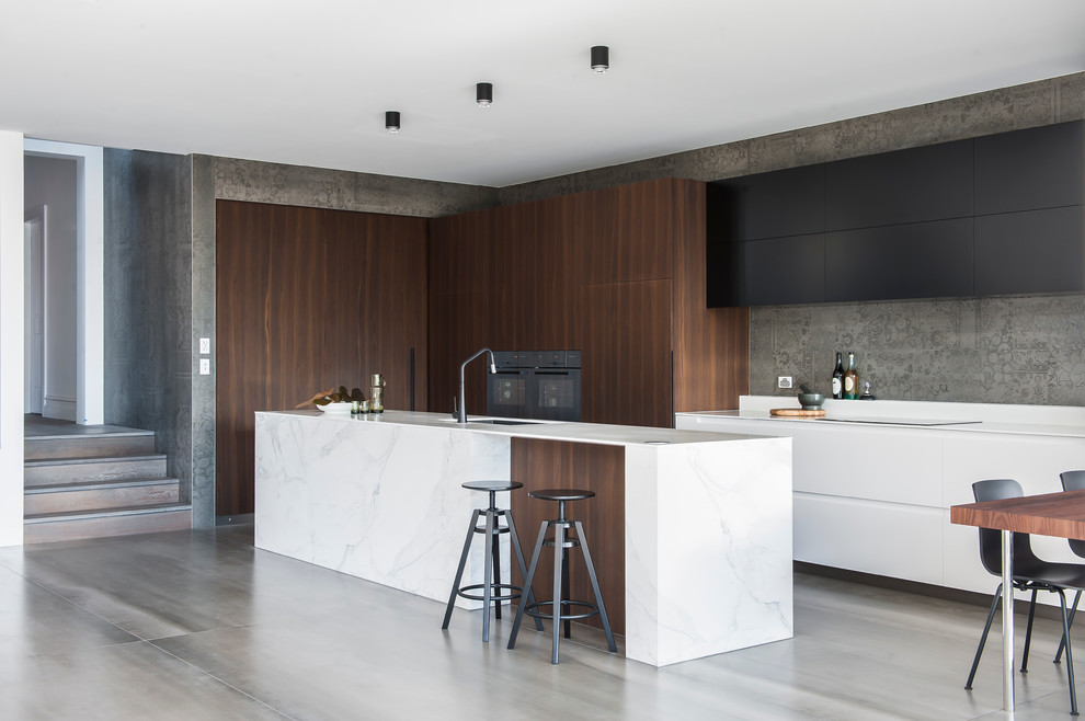 Medium sized modern l-shaped kitchen/diner in Sydney with dark wood cabinets, composite countertops, grey splashback, cement tile splashback, black appliances, ceramic flooring, an island and a submerged sink.