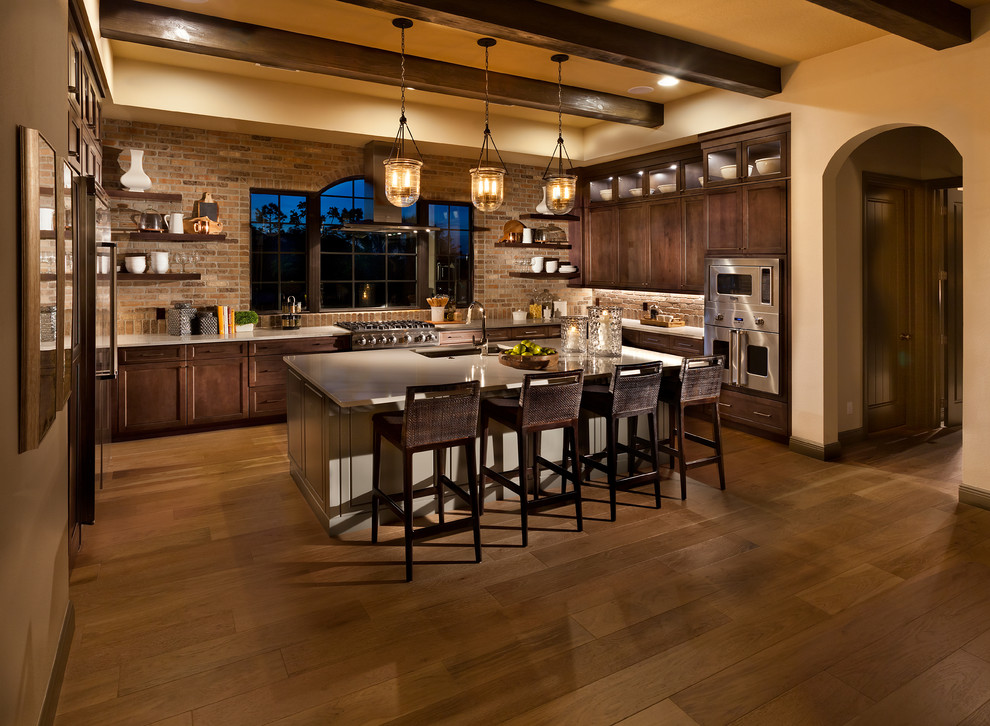 Large tuscan medium tone wood floor and brown floor kitchen photo in Tampa with solid surface countertops, brick backsplash, stainless steel appliances, an island, an undermount sink, shaker cabinets and dark wood cabinets