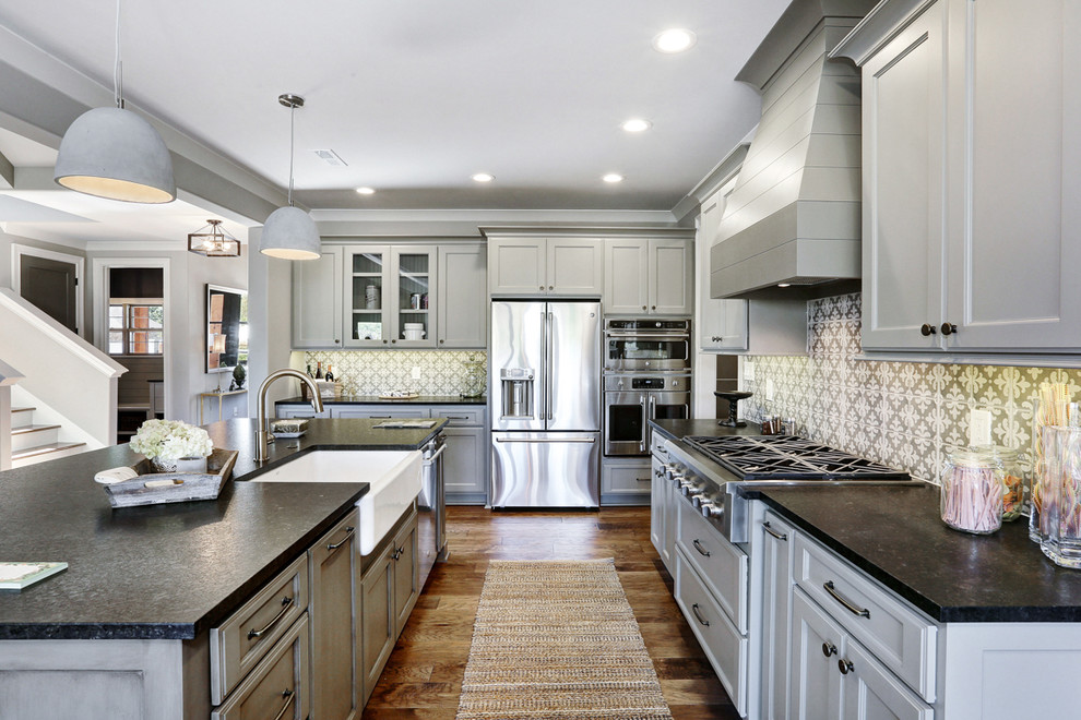 Example of a large arts and crafts l-shaped medium tone wood floor and brown floor kitchen pantry design in Other with a farmhouse sink, recessed-panel cabinets, white cabinets, granite countertops, multicolored backsplash, stone tile backsplash, stainless steel appliances and an island