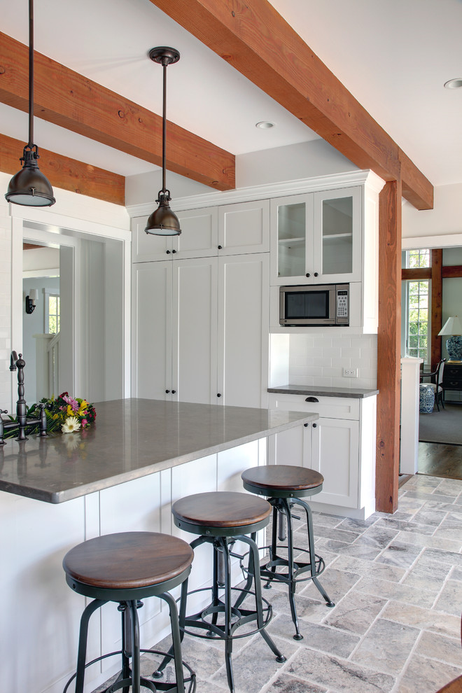 Example of a large classic u-shaped travertine floor eat-in kitchen design in Manchester with stainless steel appliances, limestone countertops, an undermount sink, shaker cabinets, white cabinets, white backsplash, subway tile backsplash and an island