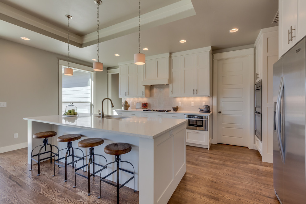 Large contemporary kitchen/diner in Boise with shaker cabinets, white cabinets, granite worktops, stainless steel appliances, light hardwood flooring and an island.