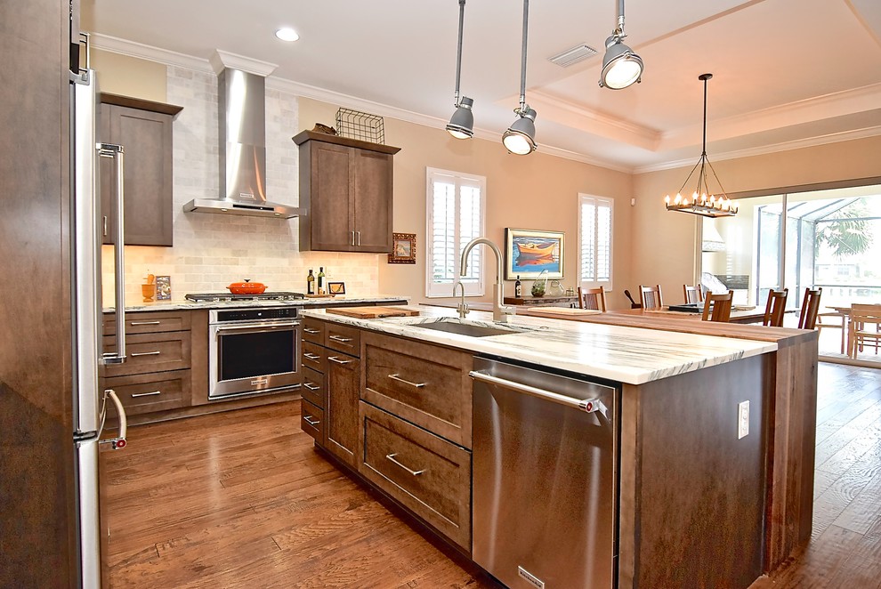 Photo of a large traditional l-shaped kitchen/diner in Tampa with a submerged sink, shaker cabinets, dark wood cabinets, marble worktops, grey splashback, marble splashback, stainless steel appliances, medium hardwood flooring, an island, brown floors and white worktops.