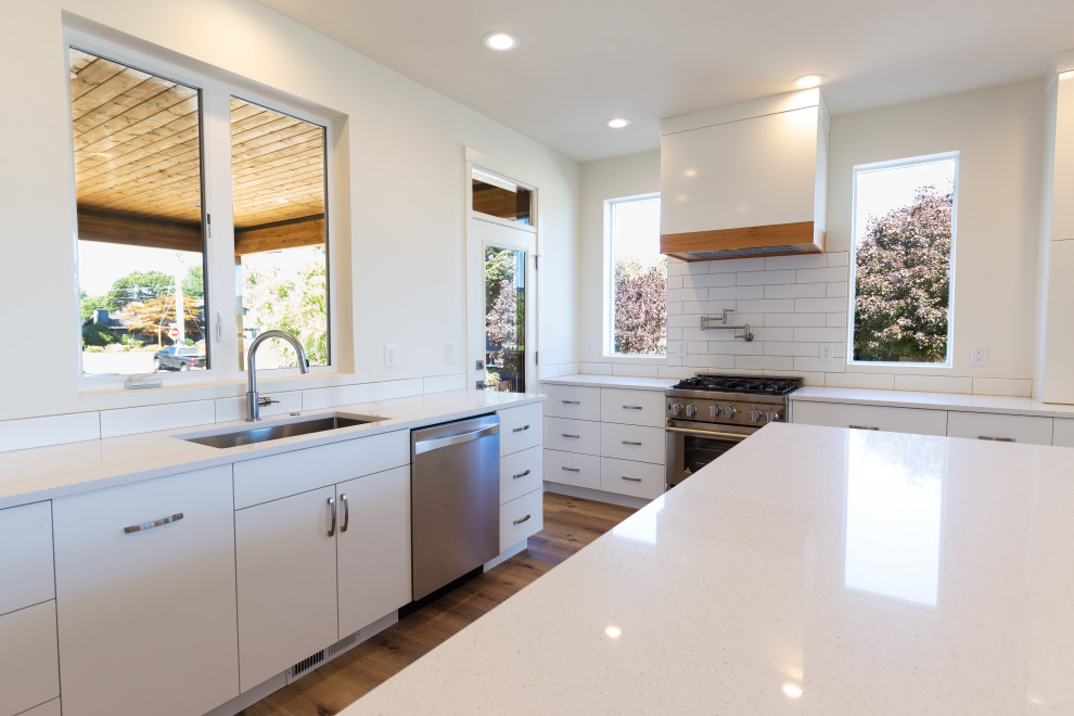 Inspiration for a large modern l-shaped light wood floor open concept kitchen remodel in Portland with an integrated sink, flat-panel cabinets, white cabinets, quartz countertops, white backsplash, ceramic backsplash, stainless steel appliances, an island and white countertops