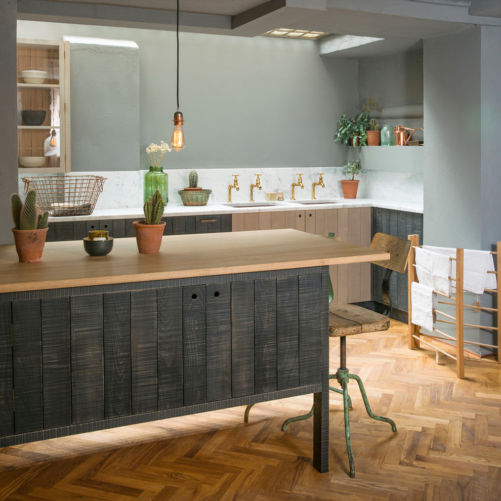 This is an example of a medium sized industrial l-shaped kitchen in London with marble worktops, medium hardwood flooring, a submerged sink, flat-panel cabinets, distressed cabinets, white splashback and stone slab splashback.