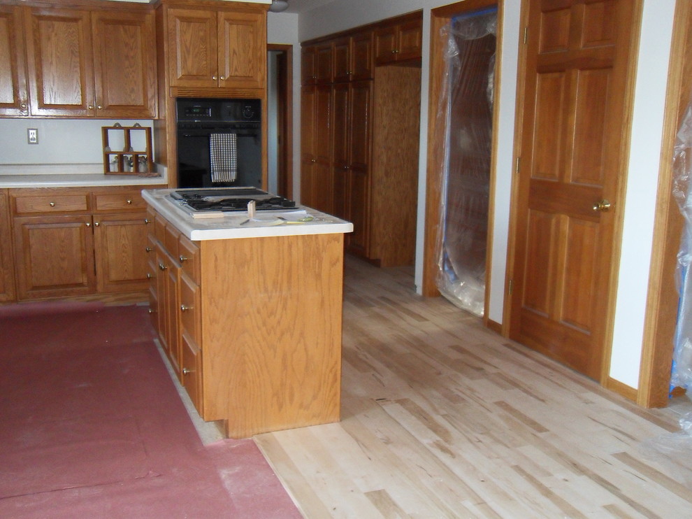 Example of a mid-sized classic u-shaped light wood floor eat-in kitchen design in Other with an undermount sink, raised-panel cabinets, light wood cabinets, granite countertops, black appliances and an island