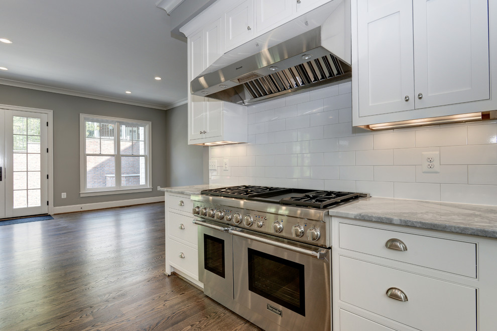 Photo of a large country u-shaped open plan kitchen in DC Metro with a submerged sink, shaker cabinets, white cabinets, quartz worktops, white splashback, metro tiled splashback, stainless steel appliances, medium hardwood flooring and an island.