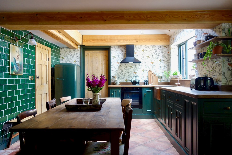 Idéer för ett mellanstort klassiskt brun kök, med en rustik diskho, skåp i shakerstil, gröna skåp, träbänkskiva, glaspanel som stänkskydd, svarta vitvaror och klinkergolv i terrakotta