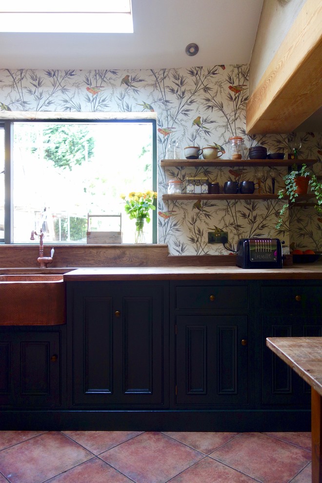 Bild på ett mellanstort vintage brun brunt kök, med en rustik diskho, skåp i shakerstil, gröna skåp, träbänkskiva, glaspanel som stänkskydd, svarta vitvaror och klinkergolv i terrakotta