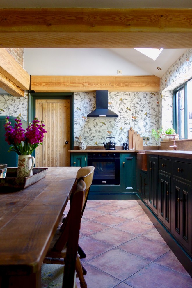 Exempel på ett mellanstort klassiskt brun brunt kök, med en rustik diskho, skåp i shakerstil, gröna skåp, träbänkskiva, glaspanel som stänkskydd, svarta vitvaror och klinkergolv i terrakotta