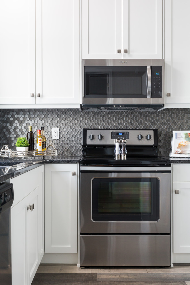Modern inredning av ett mellanstort svart svart l-kök, med en undermonterad diskho, skåp i shakerstil, vita skåp, granitbänkskiva, grått stänkskydd, stänkskydd i mosaik, rostfria vitvaror, laminatgolv, en köksö och flerfärgat golv