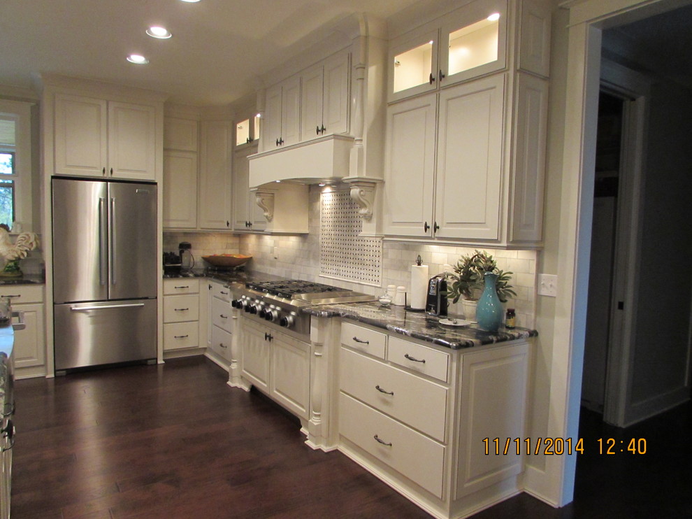 Klassisk inredning av ett mellanstort kök, med en undermonterad diskho, luckor med upphöjd panel, vita skåp, granitbänkskiva, grått stänkskydd, stänkskydd i stenkakel, rostfria vitvaror, mörkt trägolv och en köksö