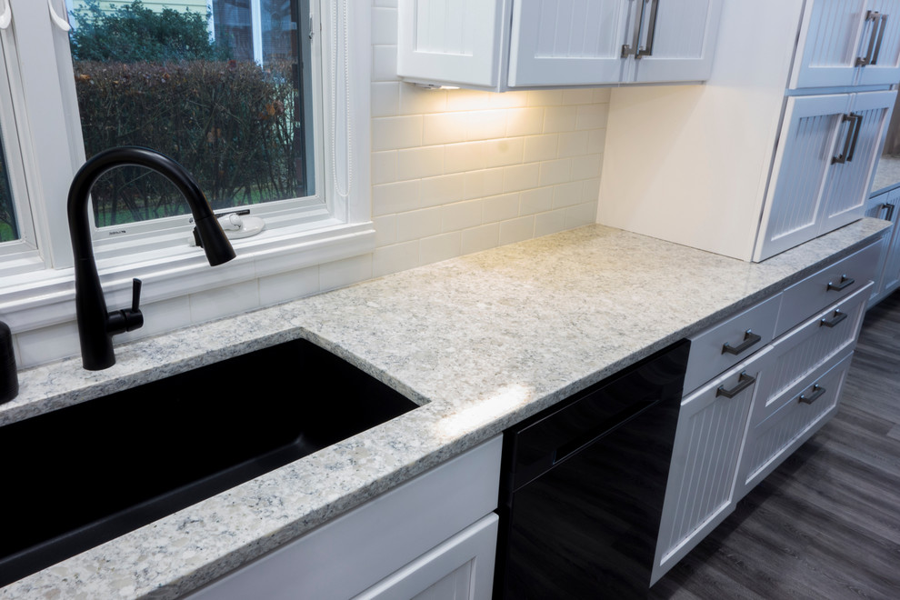 Foto på ett litet, avskilt funkis kök, med en undermonterad diskho, skåp i shakerstil, vita skåp, granitbänkskiva, vitt stänkskydd, stänkskydd i tunnelbanekakel, svarta vitvaror och mellanmörkt trägolv