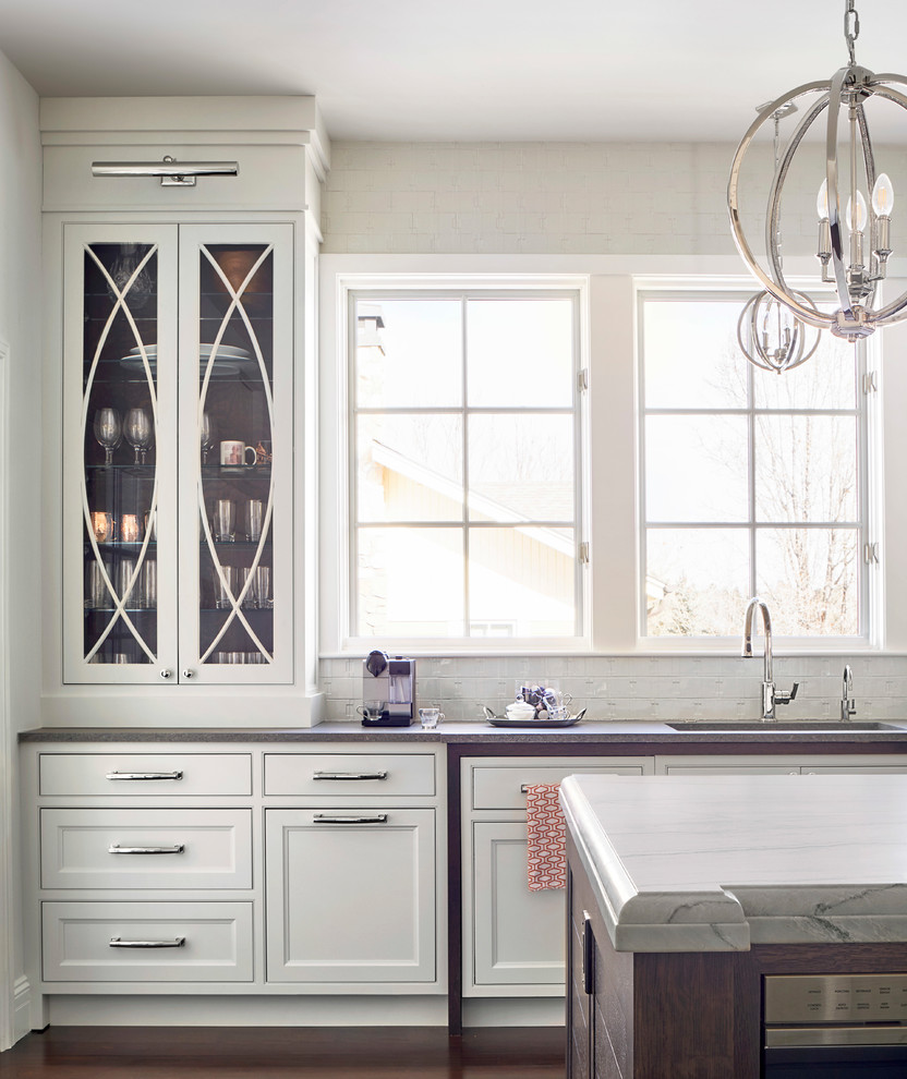 Bild på ett mycket stort vintage vit vitt kök, med en undermonterad diskho, luckor med infälld panel, vita skåp, bänkskiva i kvartsit, vitt stänkskydd, stänkskydd i keramik, integrerade vitvaror, mörkt trägolv, en köksö och brunt golv
