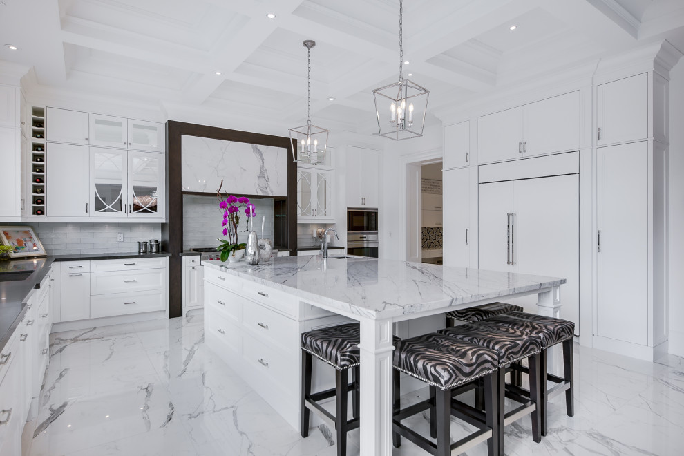 Transitional u-shaped white floor kitchen photo in Toronto with an undermount sink, shaker cabinets, white cabinets, white backsplash, stainless steel appliances, an island and gray countertops