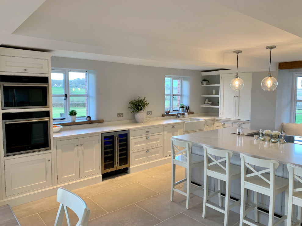 This is an example of a large traditional u-shaped open plan kitchen in Gloucestershire with a belfast sink, shaker cabinets, white cabinets, quartz worktops, ceramic flooring, an island, grey floors and white worktops.