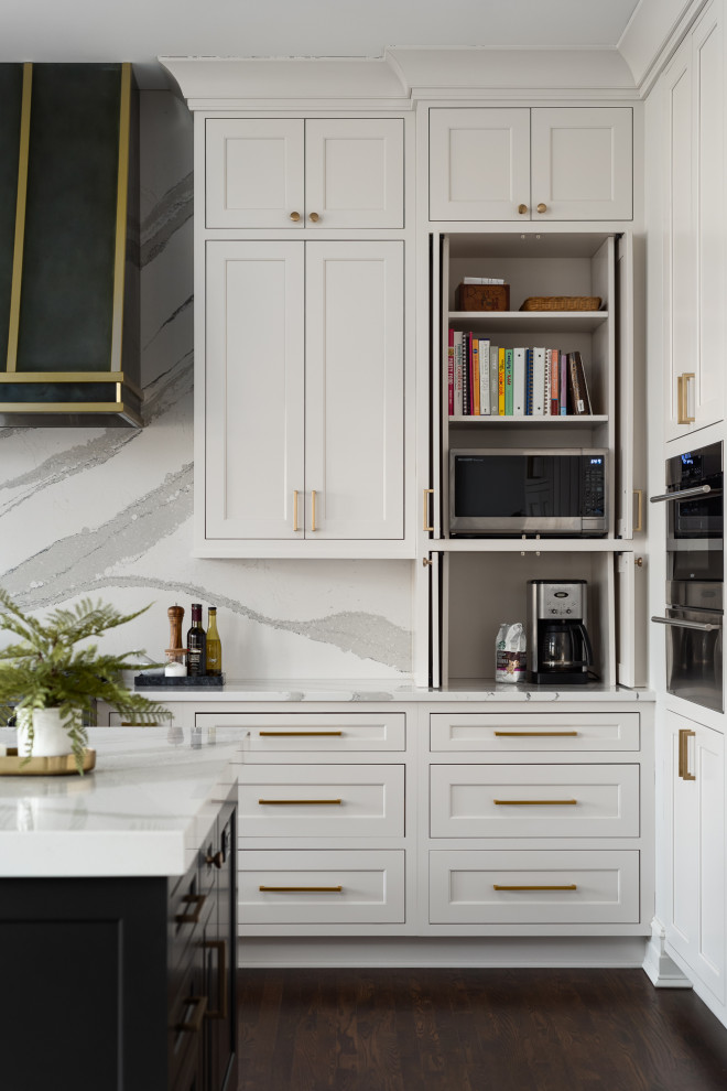 Klassisk inredning av ett stort vit vitt kök, med en undermonterad diskho, släta luckor, vita skåp, bänkskiva i kvarts, vitt stänkskydd, integrerade vitvaror, mörkt trägolv, flera köksöar och brunt golv