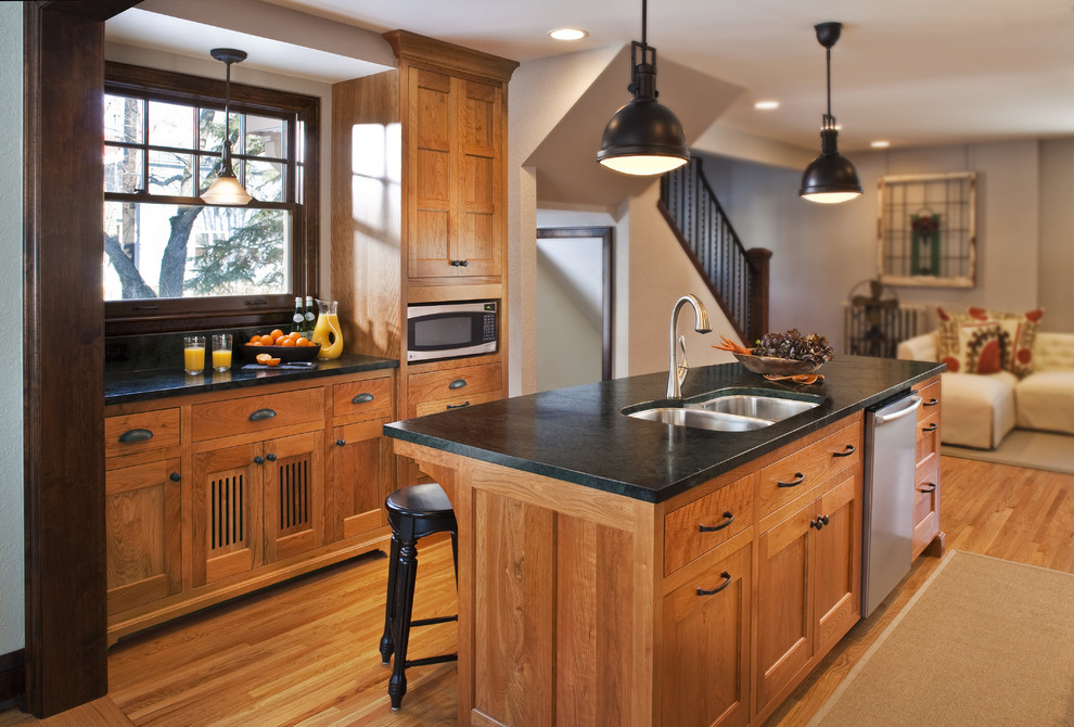 This is an example of a medium sized traditional open plan kitchen in Minneapolis with a double-bowl sink, shaker cabinets, medium wood cabinets, soapstone worktops, stainless steel appliances, light hardwood flooring and an island.