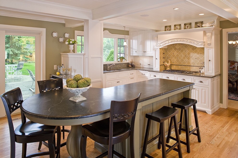 Example of a mid-sized classic l-shaped light wood floor eat-in kitchen design in Minneapolis with soapstone countertops, a double-bowl sink, raised-panel cabinets, white cabinets and an island