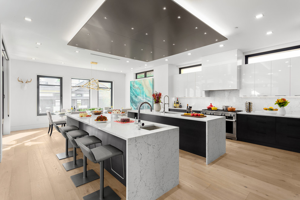 Design ideas for a large contemporary l-shaped kitchen/diner in Vancouver with a submerged sink, flat-panel cabinets, black cabinets, engineered stone countertops, white splashback, stone slab splashback, stainless steel appliances, light hardwood flooring, multiple islands, brown floors and white worktops.