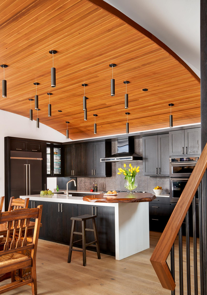 Moderne Küche in L-Form mit Schrankfronten im Shaker-Stil, dunklen Holzschränken, Küchenrückwand in Grau, Küchengeräten aus Edelstahl, hellem Holzboden, Kücheninsel, beigem Boden und weißer Arbeitsplatte in Denver