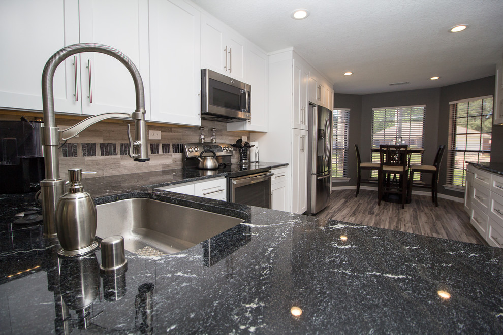Example of a mid-sized trendy u-shaped porcelain tile and gray floor eat-in kitchen design in Houston with a single-bowl sink, shaker cabinets, white cabinets, granite countertops, gray backsplash, limestone backsplash, stainless steel appliances and no island