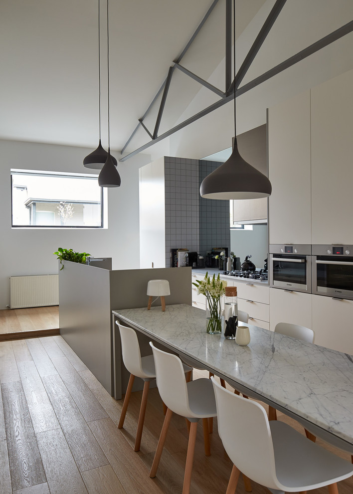 Moderne Küche mit flächenbündigen Schrankfronten, weißen Schränken, Küchengeräten aus Edelstahl und braunem Holzboden in Melbourne