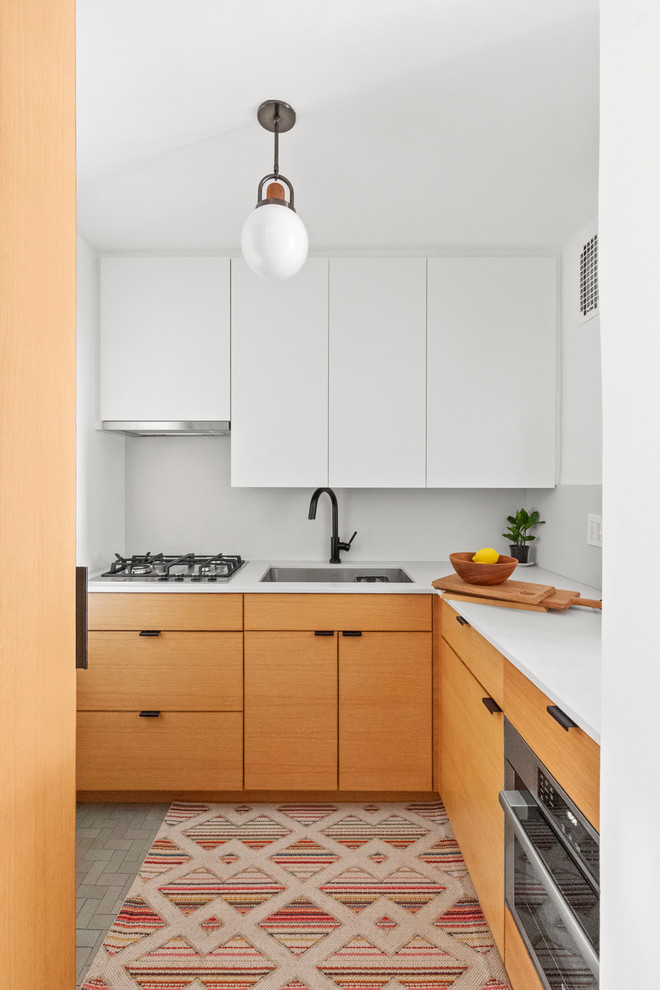 Moderne Küche in L-Form mit Unterbauwaschbecken, flächenbündigen Schrankfronten, hellbraunen Holzschränken, Küchenrückwand in Weiß, Küchengeräten aus Edelstahl, grauem Boden und weißer Arbeitsplatte in New York