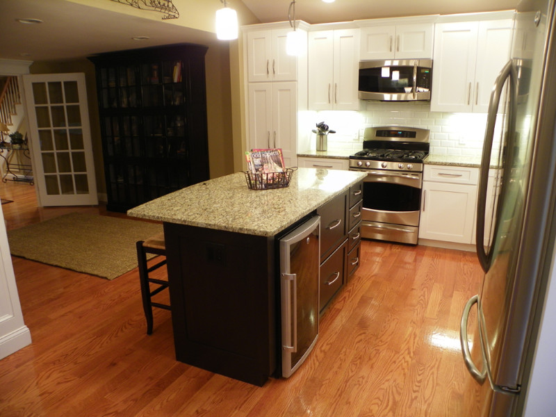 Klassisk inredning av ett mellanstort kök, med en undermonterad diskho, skåp i shakerstil, vita skåp, granitbänkskiva, vitt stänkskydd, stänkskydd i tunnelbanekakel, rostfria vitvaror, mellanmörkt trägolv och en köksö