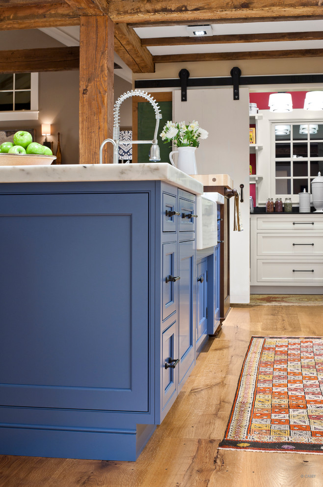 Cette image montre une cuisine ouverte parallèle traditionnelle de taille moyenne avec un placard avec porte à panneau encastré, des portes de placard bleues, plan de travail en marbre, îlot, un évier encastré et un sol en bois brun.