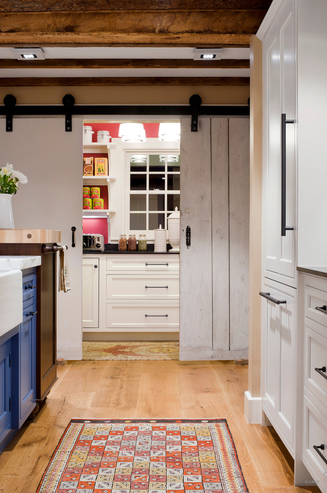 Landhaus Küche mit Landhausspüle, Kassettenfronten, blauen Schränken, Marmor-Arbeitsplatte, Elektrogeräten mit Frontblende, hellem Holzboden und braunem Boden in Boston
