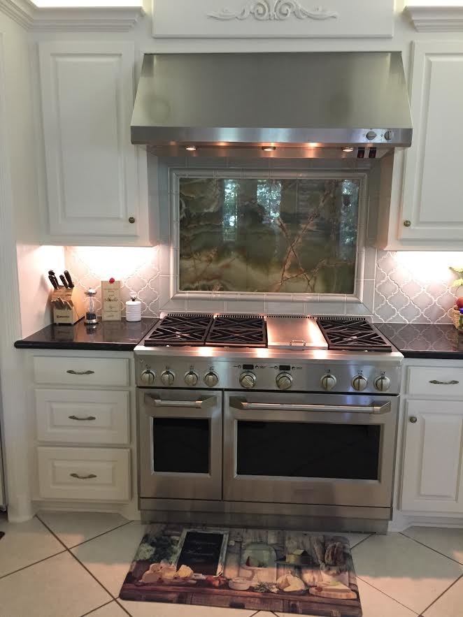 Large elegant l-shaped ceramic tile and white floor eat-in kitchen photo in Houston with a drop-in sink, raised-panel cabinets, white cabinets, solid surface countertops, blue backsplash, ceramic backsplash, stainless steel appliances and black countertops