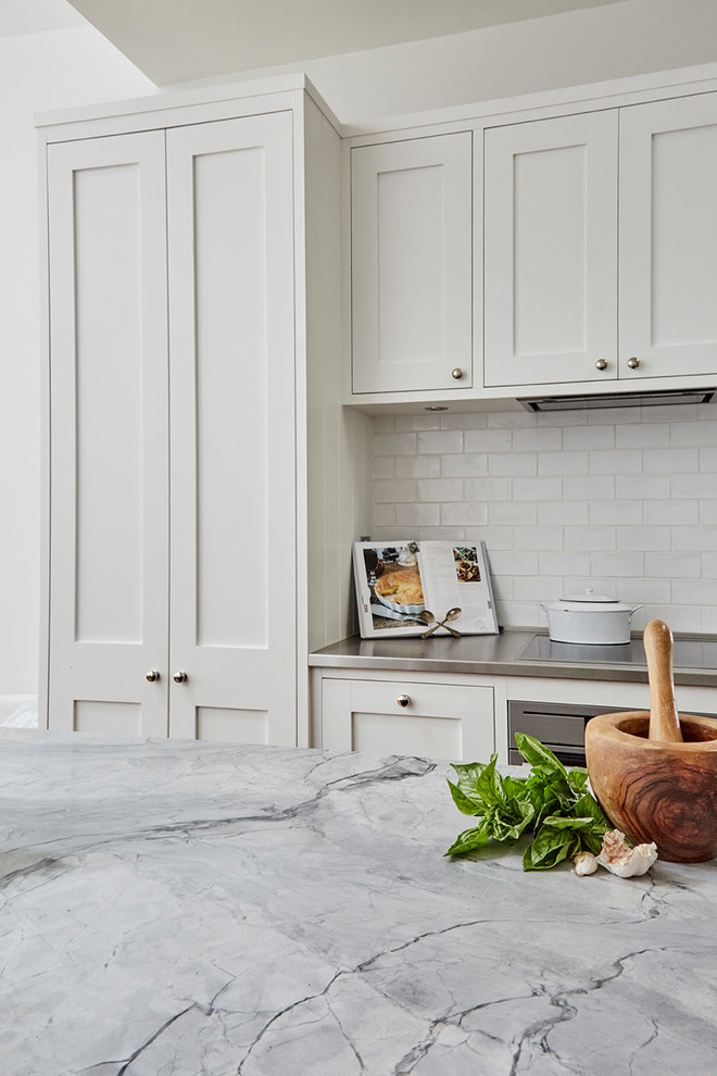 Klassisk inredning av ett mellanstort kök, med en undermonterad diskho, skåp i shakerstil, vita skåp, marmorbänkskiva, vitt stänkskydd, stänkskydd i tunnelbanekakel, rostfria vitvaror, ljust trägolv och en köksö