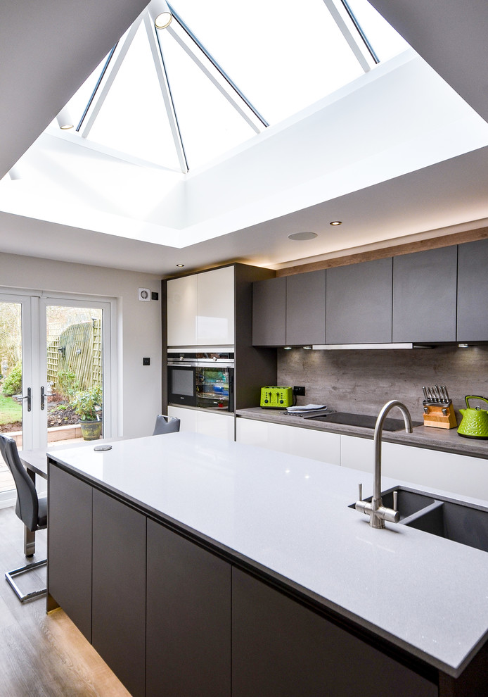 This is an example of a medium sized contemporary u-shaped kitchen/diner in Glasgow with a built-in sink, flat-panel cabinets, black cabinets, wood worktops, white splashback, wood splashback, integrated appliances, medium hardwood flooring, an island and brown floors.