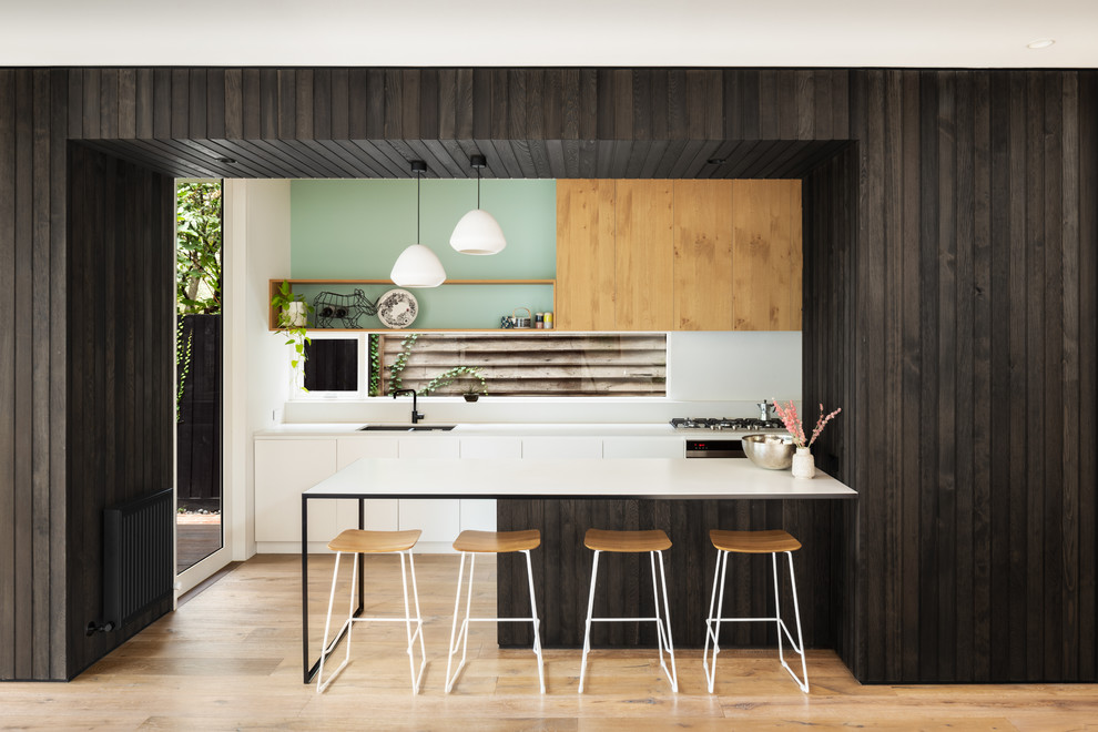 Zweizeilige Moderne Küche mit Doppelwaschbecken, flächenbündigen Schrankfronten, weißen Schränken, Küchenrückwand in Grün, Rückwand-Fenster, braunem Holzboden, Halbinsel, braunem Boden und weißer Arbeitsplatte in Melbourne