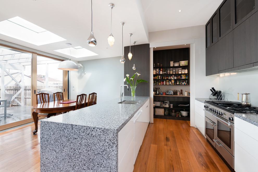 Inspiration for a contemporary galley eat-in kitchen remodel in Melbourne with a double-bowl sink, flat-panel cabinets, white cabinets, white backsplash, glass sheet backsplash and stainless steel appliances